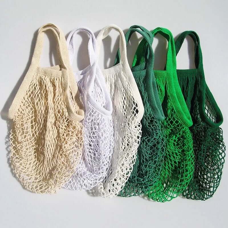 Set of eco-friendly organic cotton mesh bags in natural beige, white, and green colors for sustainable shopping.