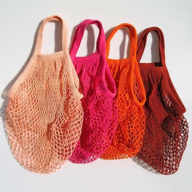 Four eco-friendly organic cotton mesh bags in shades of peach, pink, orange, and brown on a white background.