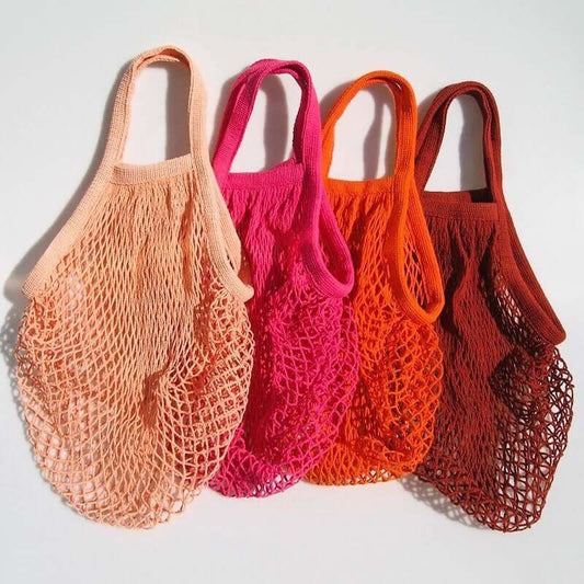Four eco-friendly organic cotton mesh bags in shades of peach, pink, orange, and brown on a white background.