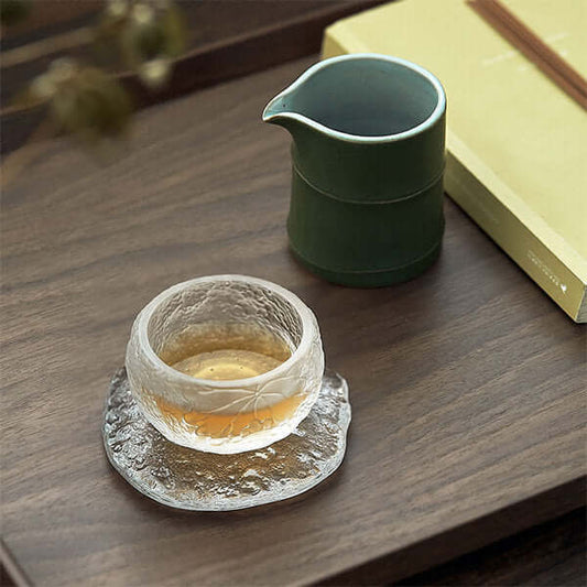 Elegant green bamboo ceramic cup beside a textured glass teacup on a wooden tray, showcasing a serene tea setting.