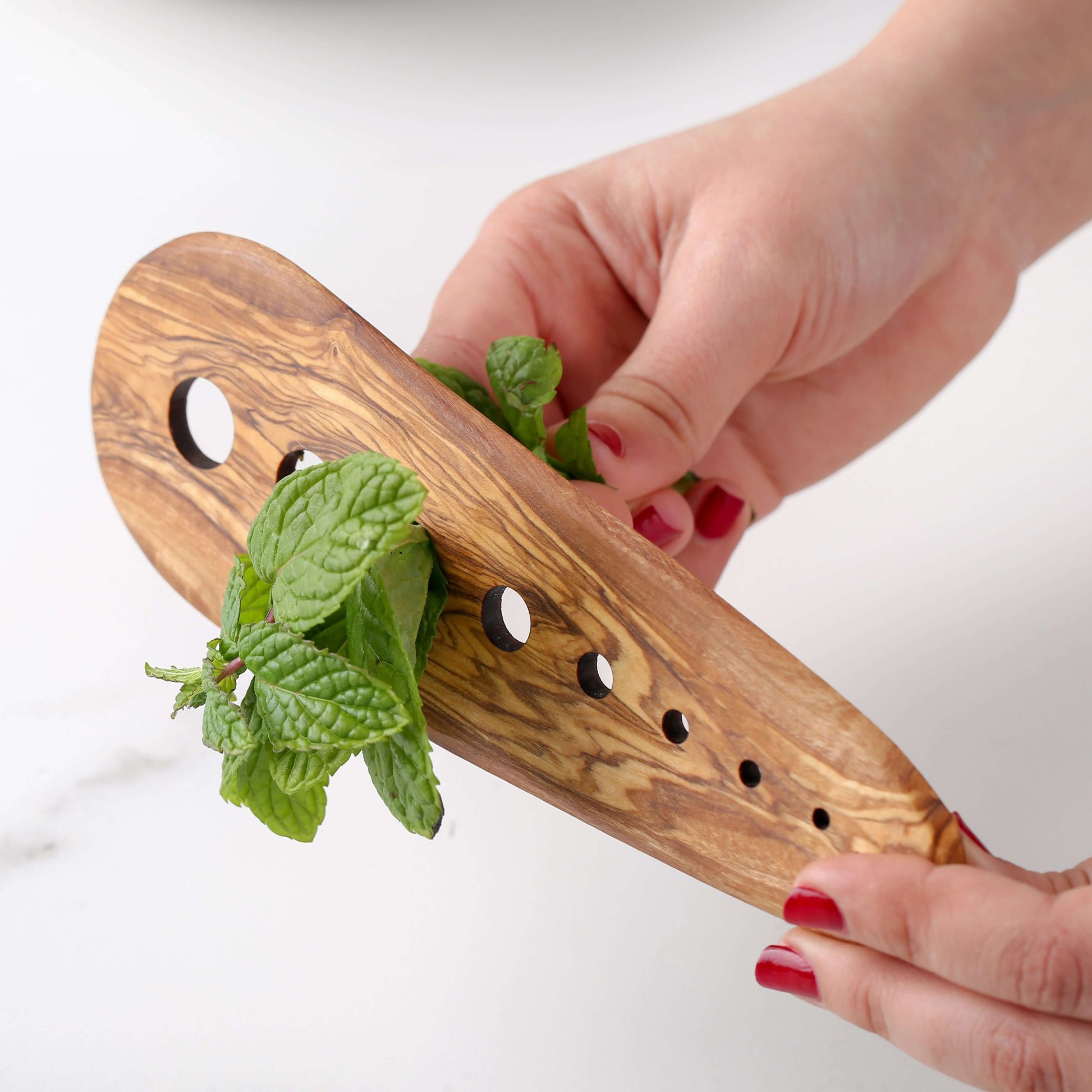 Hand holding an olive wood herb stripper with fresh mint, showcasing eco-friendly kitchen accessory features.