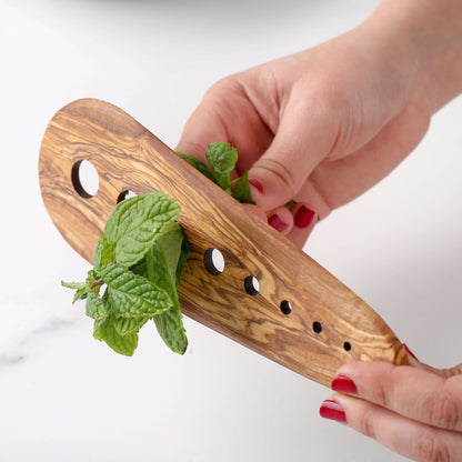 Hand holding an olive wood herb stripper with fresh mint, showcasing eco-friendly kitchen accessory features.