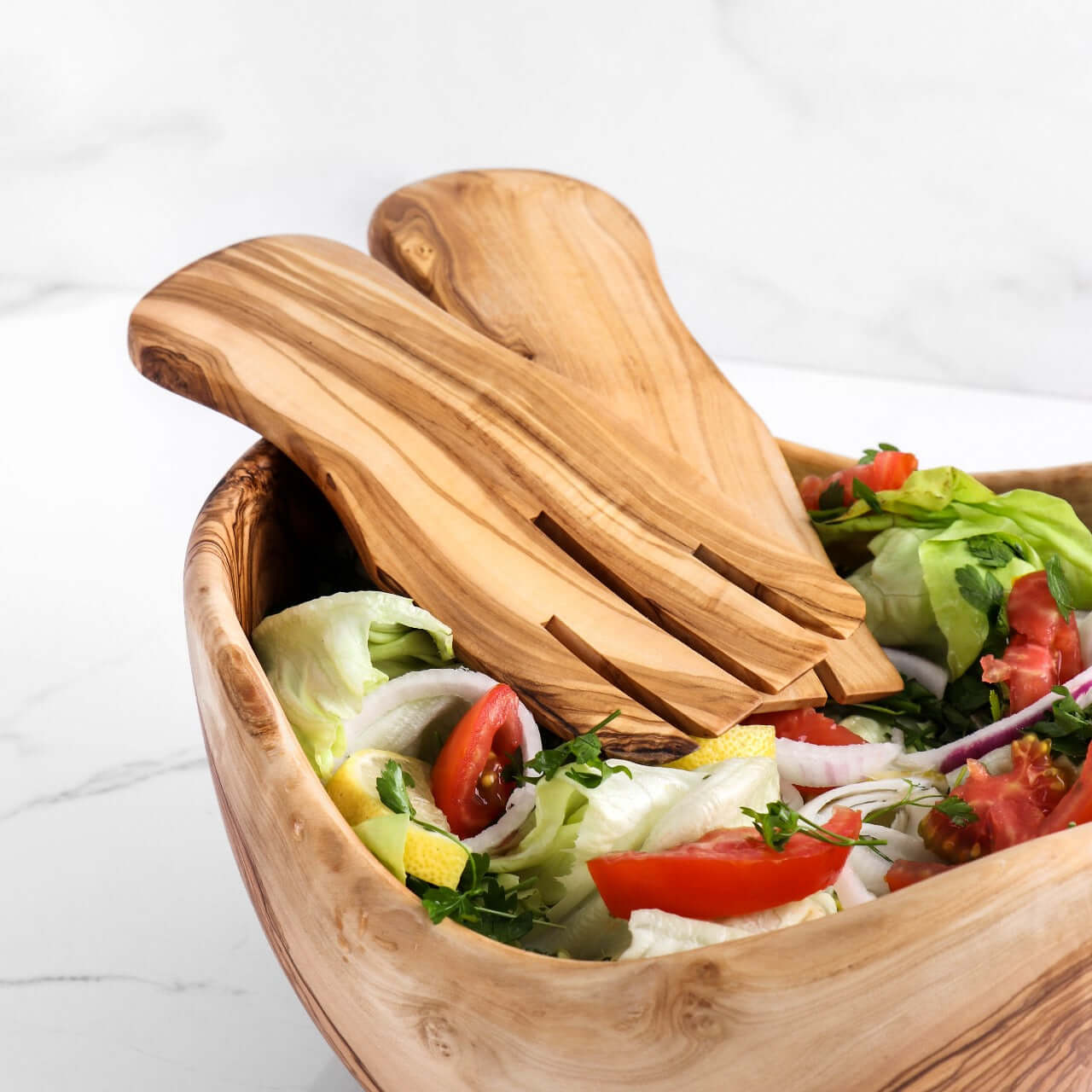 Handmade olive wood salad hands resting in a salad bowl with fresh greens and vegetables, ideal for eco-friendly entertaining.