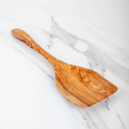 Handmade olive wood shovel spoon on a marble countertop, ideal for stirring and serving dishes.