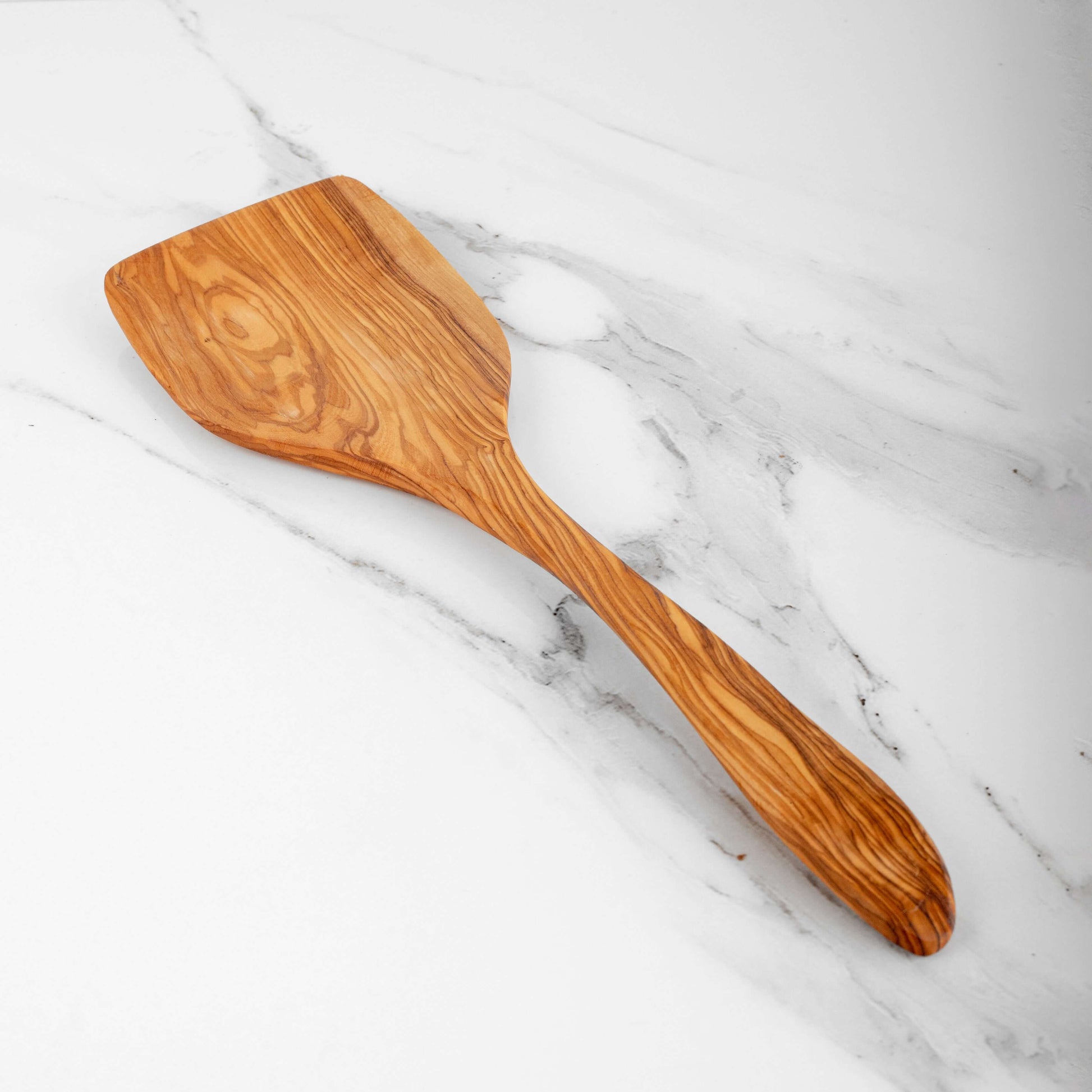 Handmade olive wood shovel spoon on marble surface, ideal for stirring and serving with elegant design.