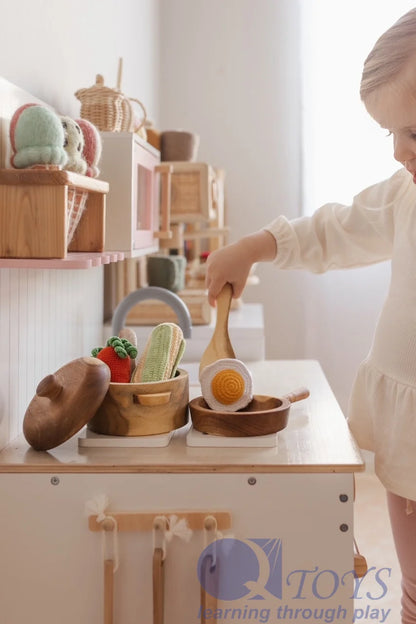 Child playing with wooden cooking toys, including pots and utensils, promoting imaginative play and creativity.