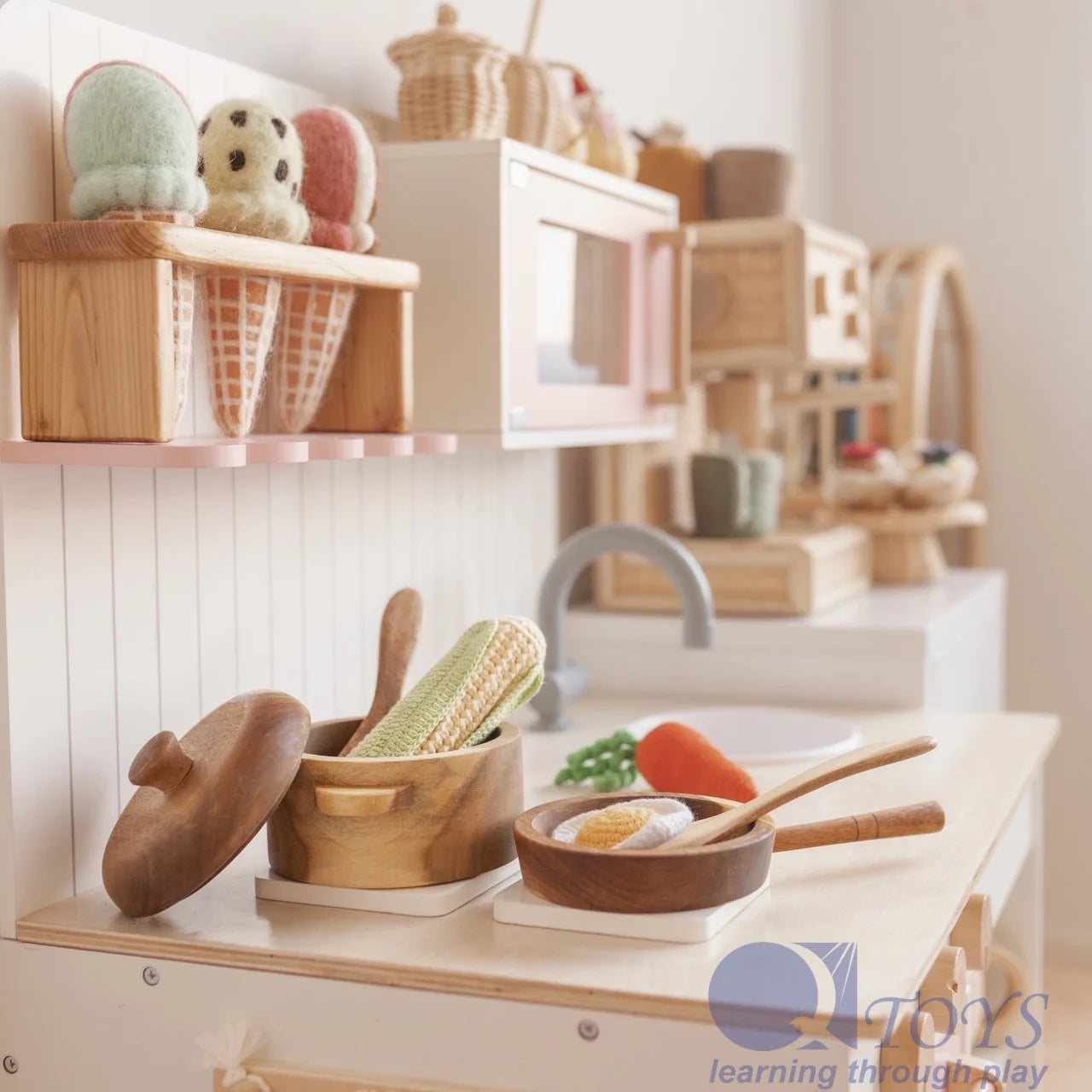 Stylish mahogany toy pot and pan set on a play kitchen countertop with colorful felt vegetables.