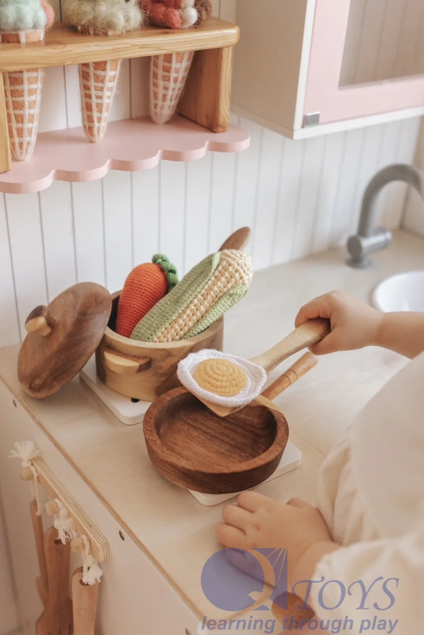Child playing with wooden cooking toys, featuring a mahogany pot and colorful wooden food items.