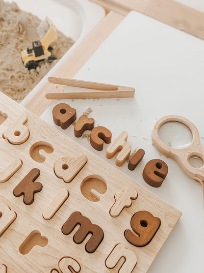 Natural lower case letter puzzle pieces arranged on a wooden board for educational play.