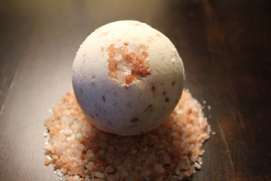 Organic bath fizzie on a wooden surface, surrounded by bath salts for a detox experience.