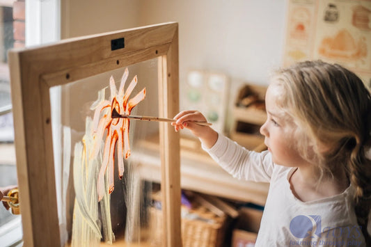 Toddler painting a sun on a double-sided perspex easel, promoting creativity and motor skills.
