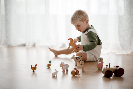 Toddler playing with a wooden farm animals and tractor play set, fostering creativity and pretend play.