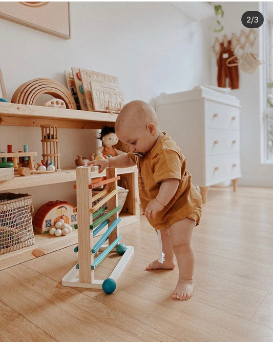 Toddler playing with a wooden ball run toy, promoting motor skills and hand-eye coordination.