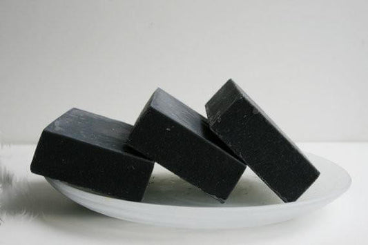 Three bars of unscented activated charcoal soap stacked on a white plate, ideal for sensitive skin and pore cleansing.