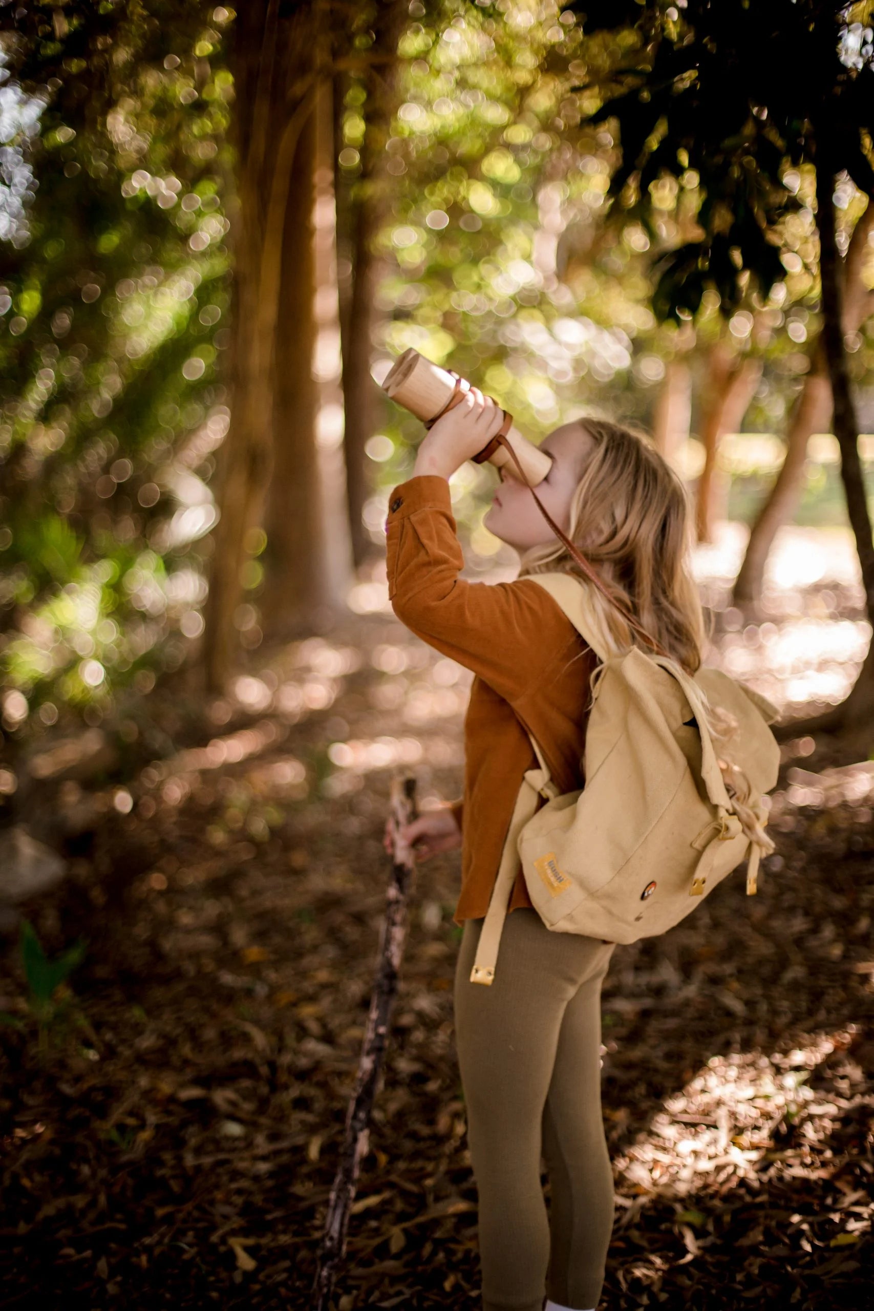 Child exploring nature with wooden binoculars, promoting imagination and adventure in a forest setting.